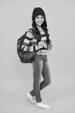 Funny school girl child student with backpack and warn hat, isolated yellow background. Learning and knowledge education concept. Autumn school. Happy teenager, positive and smiling