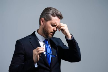 Üzgün adamın ağrıdan dolayı migreni tuttu. Başı ağrıyan takım elbiseli adam gri stüdyoda izole edilmiş. Başı ağrıyan serbest çalışan ya da menajer. Stresli, yorgun iş adamı baş ağrısından