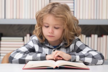 Kid reading a book in a school library. School boy education concept