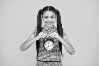 Portrait of teenage girl with clock alrm, time and deadline. Studio shot isolated on yellow background. Happy teenager, positive and smiling emotions of teen girl