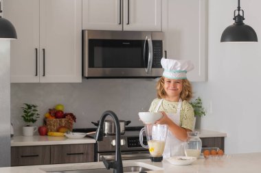 Çocuk aşçı ev mutfağında pasta yapmayı öğreniyor. Çocuk lezzetli yapıyor. Aşçı şapkalı küçük çocuk ve mutfakta yemek pişiren önlük.