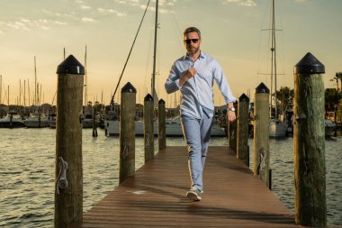 Yatın yanında zengin bir iş adamı var. Moda erkek modelinin açık havada portresi. Yatların yanında poz veren zengin bir erkek. Şehir tarzında zengin bir adam. Yat kulübündeki zengin adam. Lüks yat gemilerinin yakınındaki körfezde bir adam.