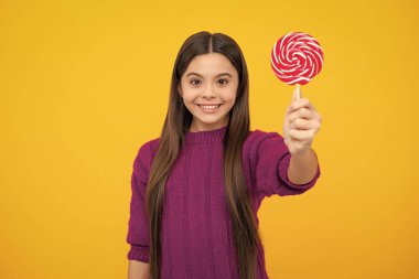 Teen girl hold lollipop caramel on yellow background, candy shop. Teenager with sweets suckers