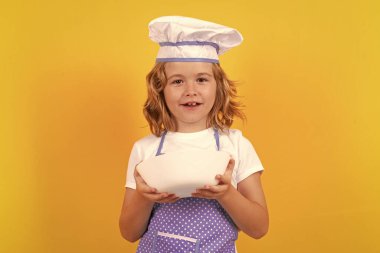 Mutfak tabağıyla komik aşçı çocuk, stüdyo portresi. Çocuk aşçı, stüdyo resmi. Çocuklar yemek yapıyor. Önlüklü ve aşçı şapkalı genç çocuk.