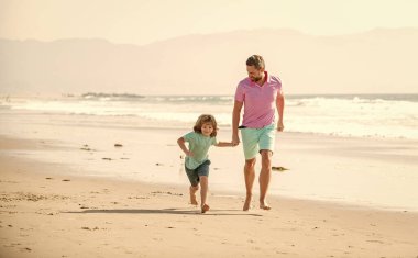 Baba ve çocuk dışarıda eğleniyorlar. Çocukluk ve ebeveynlik. Gülümseyen baba ve oğul yaz plajında koşuyor. Aile seyahati ve tatil. Babalar ya da aile günü. Baba ve çocuk yaz günü.