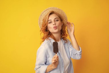 Genç kadın lezzetli dondurma yiyor, dondurulmuş tatlıyı seviyor, günlük kıyafetler giyiyor, sarı arka planda izole edilmiş.