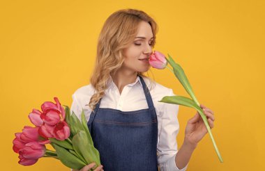 Sarı arka planda bahar lale çiçekleriyle önlükle gülümseyen genç bir kadın..