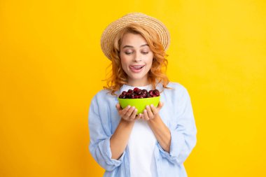 Genç bir kadın tatlı kiraz yiyor. Sarı arka planda kirazlı güzel bir kızın portresi. Yaz meyve toplama mevsimi. Doğal vitaminler