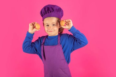 Çocuk aşçı yumurtaları tutar. Çocuk pişirme, küçük şef yemek hazırlıyor. Pembe stüdyodaki aşçı şapkalı ve önlüklü çocuk izole edilmiş arka plan.