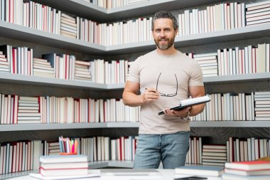 Kütüphane sınıfındaki öğretmenin portresi. Üniversite kütüphanesinde yakışıklı bir öğretmen. Öğretmenler Günü. Öğretmen ders veriyor. Kütüphanede öğretmen. Üniversite kütüphanesinde ders veriyorum.