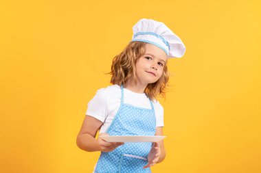Mutfak tabağıyla komik aşçı çocuk, stüdyo portresi. Şef çocuk sağlıklı yemek hazırlıyor. Şef şapkalı bir çocuğun stüdyo portresi.
