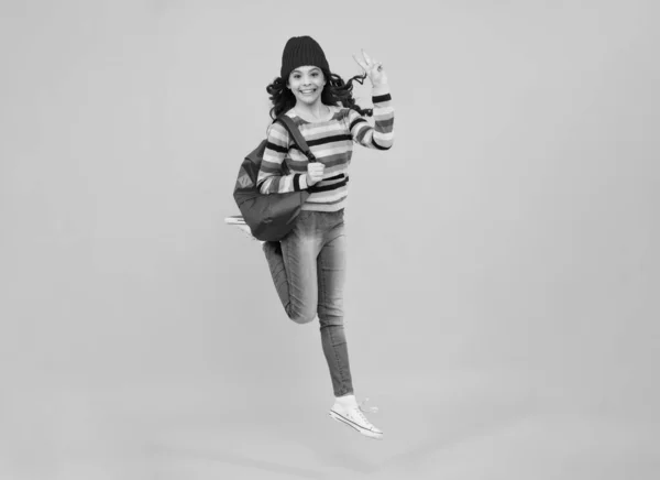 School children in winter hat and sweater with school bag on isolated yellow studio background. Children learning and education. Crazy jump and run, jumping kids