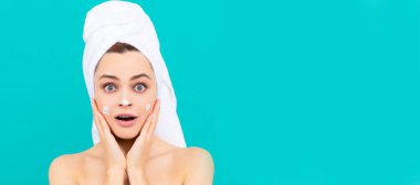 Genç bir kadının mavi arka plana yüz kremi sürmesine şaşırdım. Güzel kadın, izole edilmiş yüz portresi, taklit alanı olan pankart.