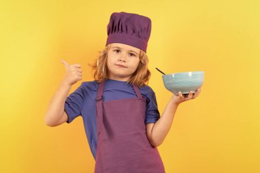Kid chef cook with cooking bowl. Kid in cooker uniform and chef hat preparing food on studio color background. Cooking, culinary and kids food concept