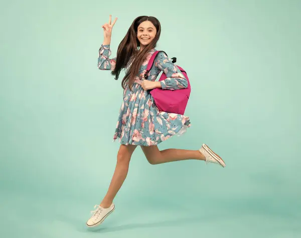 Schoolgirl in school uniform with school bag. Schoolchild, teen student hold backpack on blue isolated background. Run and jump. Happy teenager, positive and smiling emotions