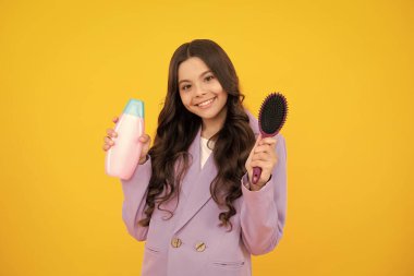 Sarı arka planda şampuan şişesi ya da duş jeli olan genç bir kız çocuğu. Çocukların saçı kozmetik üründür. Mutlu yüz, pozitif ve gülümseyen genç kız duyguları