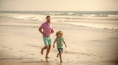 Baba ve çocuk dışarıda eğleniyorlar. Çocukluk ve ebeveynlik. Baba oğul kumsalda koşuyor. Aile seyahati ve tatil. Babalar ya da aile günü. Baba ve çocuk yaz günü.