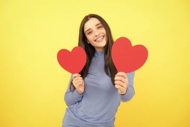 Sevgililer Günü. Ellerinde kalbi olan güzel genç bir kadın. Sarı arka planda kağıt kalpli çekici bir kadın.