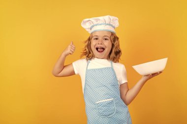 Funny kid chef cook with kitchen plate, studio portrait. Cooking children. Chef kid boy making healthy food. Portrait of little child in chef hat isolated on studio background. Kid chef