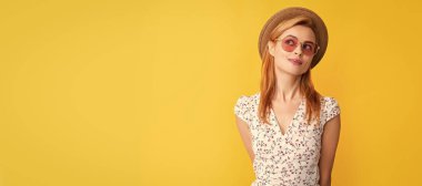 dreaming young woman in straw hat and sunglasses on yellow. Woman isolated face portrait, banner with copy space background