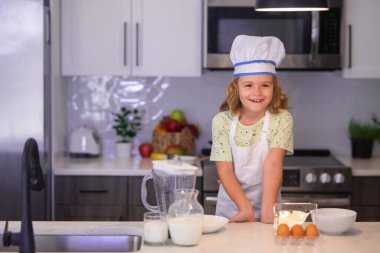 Funny kid chef cook cookery at kitchen. Chef kid boy making healthy food. Portrait of little child in chef hat