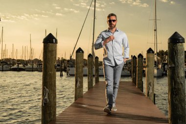 Yatta kendine güvenen yakışıklı bir adamın portresi. Yat kulübü. Moda gömlekli seksi adam yatın yanında poz veriyor. Şehirde başarılı bir erkek manken. Beyaz, orta yaşlı bir adam lüks yatın yanında.