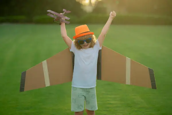 Kid pilot aviator with with paper wings dreams of traveling in summer in park outdoor