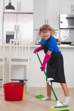 Çocuk ev konseptiyle temizlik yapıyor. Ev işlerine yardım etmek için paspasla çocuk temizliği. Küçük sevimli çocuk mutfak arka planında temizlik yapıyor.