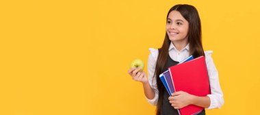 Okula tekrar hoş geldin. Elma ve kitap tutan mutlu çocuk gülümsemesi. Öğrenci portresi, stüdyo afişi. Okul çocuğu yüzü, boşluklar