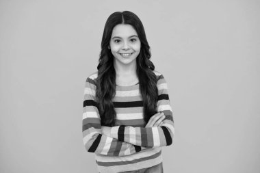 Happy teenager, positive and smiling emotions of teen girl. Teenager girl crossed arms isolated on yellow background. Studio portrait of child with mock up copy space