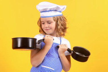 Aşçı çocuk tencereyle yemek pişiriyor. Üniformalı çocuk. Şef çocuk sarı arka planda izole edilmiş. Aşçı olmak için sevimli bir çocuk. Aşçı şapkası giymiş bir çocuk.