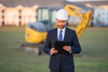 Kazıcının yanında inşaat işçisi. Evin önünde kendine güvenen bir inşaat sahibi. Mimar, inşaat mühendisi. İnşaat alanında güvenlik yeleği ve kasketi olan bir inşaat sahibi.