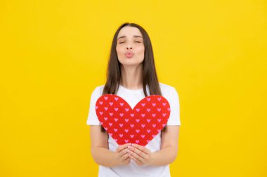 Genç bir kadın sevgililer günü konsepti, kalp şeklinde kartı olan bir kız. Sarı arka planda izole edilmiş sevgi sembolü el ele tutuşan sevimli bir kız.