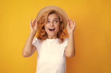 Expressive girl with surprised face. Young redhead woman in straw hat, surprised expression, isolated on yellow background. Summer lifestyle studio portrait