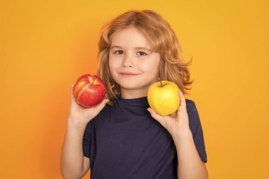 Kids face with fruits. Kid with apple in studio. Studio portrait of cute child hold apple isolated on yellow background