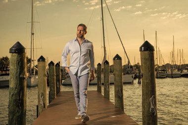 Yatta kendine güvenen yakışıklı bir adamın portresi. Yat kulübü. Moda gömlekli seksi adam yatın yanında poz veriyor. Şehirde başarılı bir erkek manken. Beyaz, orta yaşlı bir adam lüks yatın yanında.