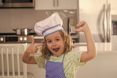Funny kid chef cook cookery at kitchen. Chef kid boy making healthy food. Portrait of little child in chef hat