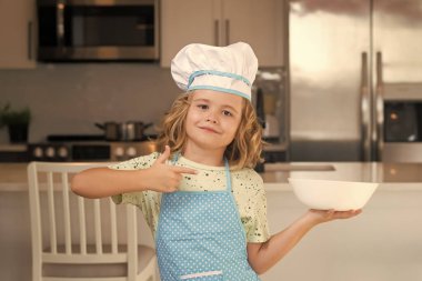 Fun kids kitchen. Funny little kid chef cook wearing uniform cook cap and apron cooked food in the kitchen. Kids are preparing food, bake cookies in the kitchen