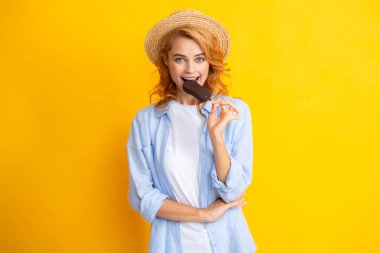 Moda portresi, sarı arka planda dondurması olan havalı genç bir kadın. Genç küstah hippi kız sopa için dondurma yiyor.