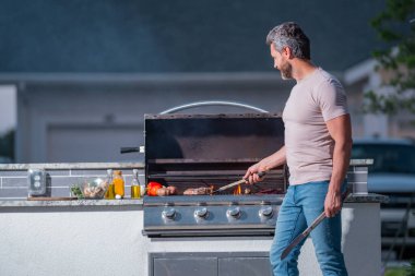 Erkek aşçı bahçede ızgara yapıyor. Barbekü açık hava bahçe partisi. Yakışıklı adam barbekü eti hazırlıyor. Yaz boyunca dışarıda yemek ve yemek pişirme kavramı