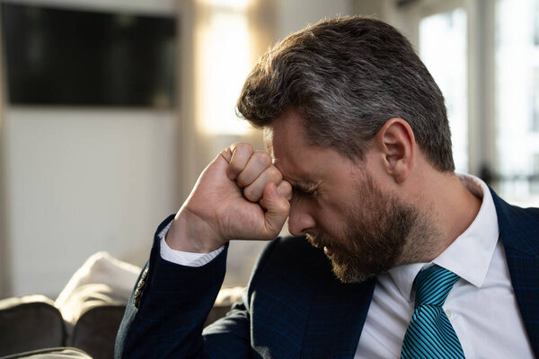 Перегруженный работой человек чувствует мигрень в голове. У утомленного бизнесмена офисный синдром. Уставший мужчина с мигренью или головной болью. Офисный работник, менеджер или фрилансер с головной болью