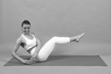 Altılı karın kası eğitimi. Spor giyimli genç bir kadın paspasın üzerinde spor yapıyor, güzel bir kız egzersiz yapıyor, gri stüdyo geçmişi üzerinde çalışıyor.