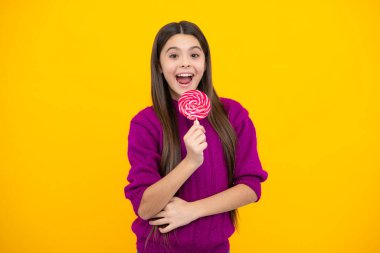 Excited face. Child eat lollipop popsicle over yellow isolated background. Yummy caramel, candy shop. Amazed expression, cheerful and glad