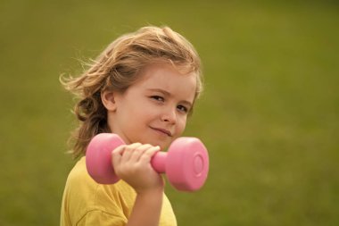 Çocuk spor egzersizleri. Sağlıklı çocuk hayatı ve spor anlayışı. Dambıllarla çalışan çocuk portresi. Çocuklar için motivasyon ve spor kavramı