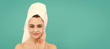 smiling young lady apply face cream on blue background. Beautiful woman isolated face portrait, banner with mock up copy space