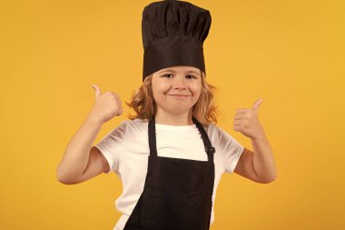 Child wearing cooker uniform and chef hat preparing food on kitchen, studio portrait. Cooking, culinary and kids food concept