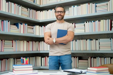 Kütüphane sınıfındaki öğretmenin portresi. Üniversite kütüphanesinde yakışıklı bir öğretmen. Öğretmenler Günü. Öğretmen ders veriyor. Kütüphanede öğretmen. Üniversite kütüphanesinde ders veriyorum.