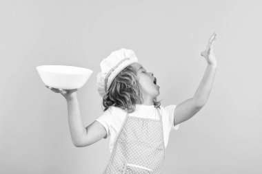 Mutfak tabağıyla komik aşçı çocuk, stüdyo portresi. Aşçı üniformalı çocuk ve aşçı şapkası stüdyo renginde yemek hazırlıyor. Aşçılık, aşçılık ve çocuk maması konsepti.