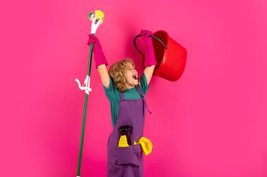 Portrait of funny child cleaning. Housekeeping and home cleaning concept. Child use duster and gloves for cleaning. Studio isolated pink background