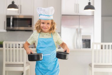 Aşçı çocuk mutfakta aşçılık yapıyor. Yemek pişirme, aşçılık ve çocuklar. Aşçı şapkalı ve önlüklü küçük çocuk.